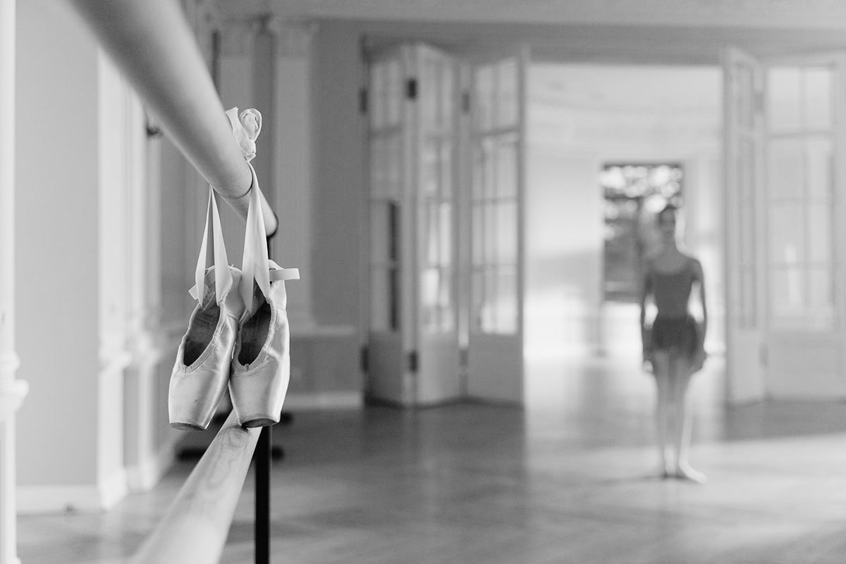 ballet shoes hanging on the barre, ballerina standing off in the distance